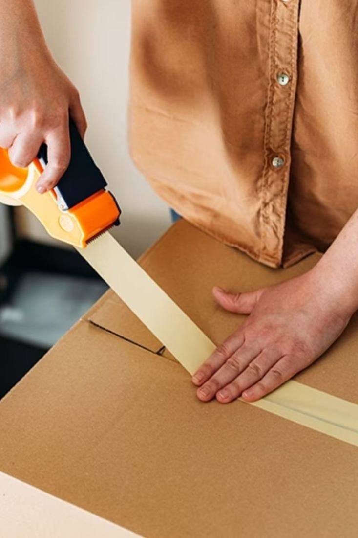 Packer sealing a cardboard carton with tape during professional packing